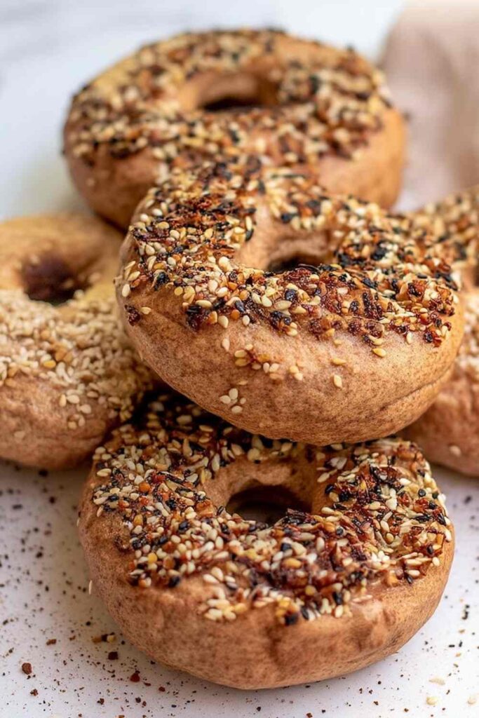 Vertical stack of everything-seasoned Thomas' high protein bagels on white surface, close-up showing texture