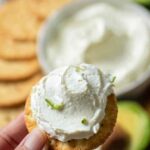 Close-up of hand holding a cracker topped with whipped cream cheese and lime zest