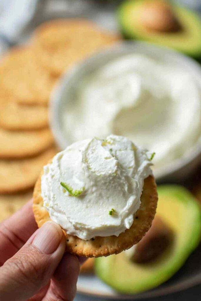 Close-up of hand holding a cracker topped with whipped cream cheese and lime zest
