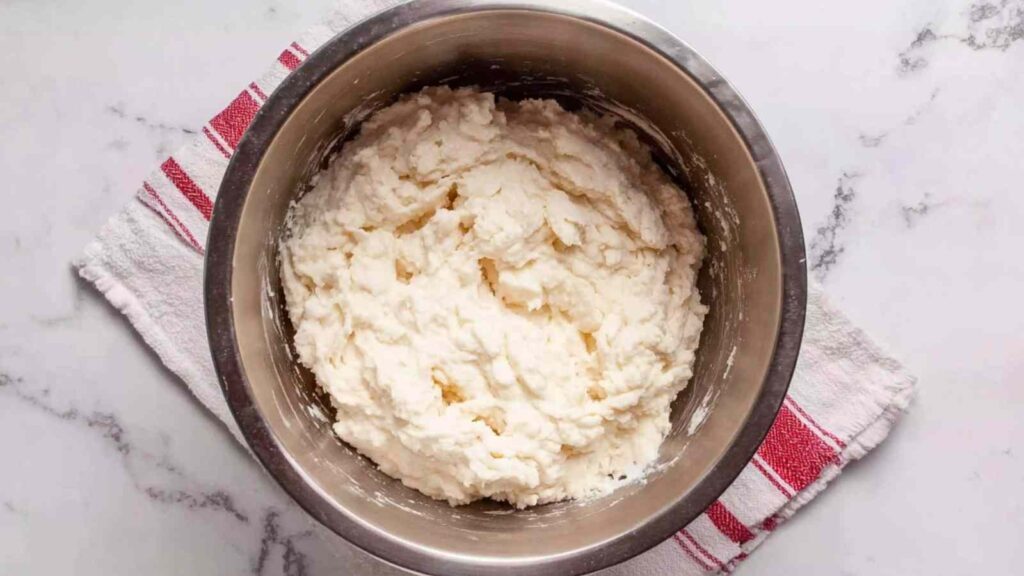 Metal mixing bowl filled with fluffy whipped egg whites on a red-striped towel, ready for baking