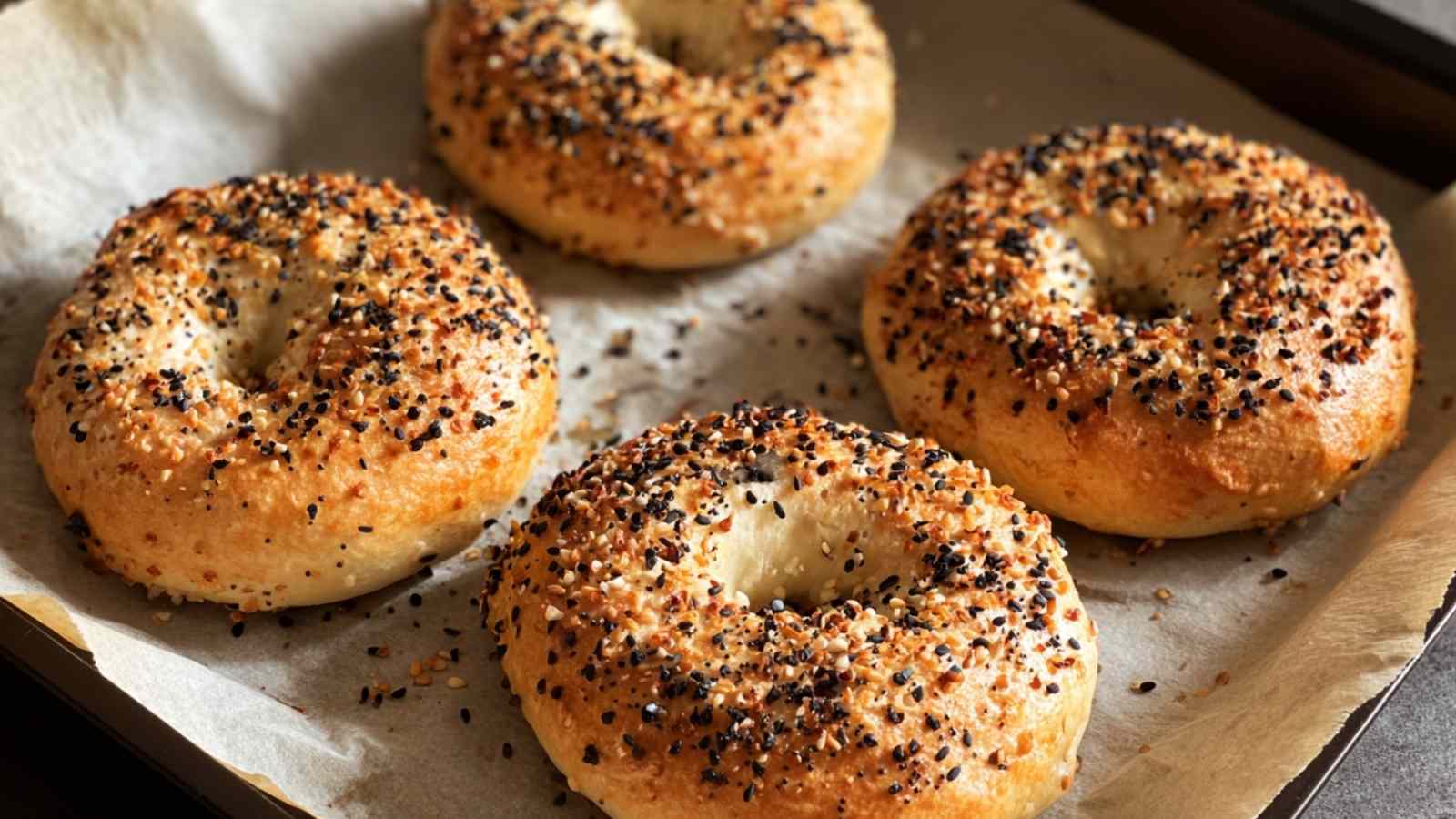 Freshly baked Greek yogurt bagels topped with everything bagel seasoning, golden brown on a parchment-lined baking sheet.