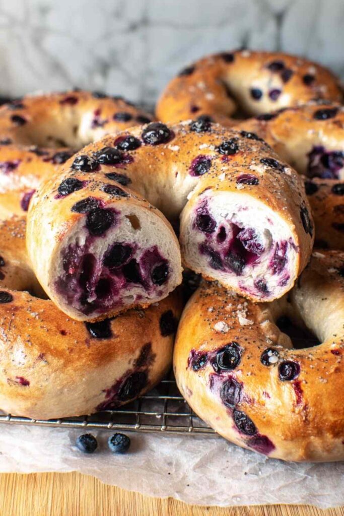 Blueberry bagel cut open on a wire rack, showing juicy berries and fluffy texture inside.