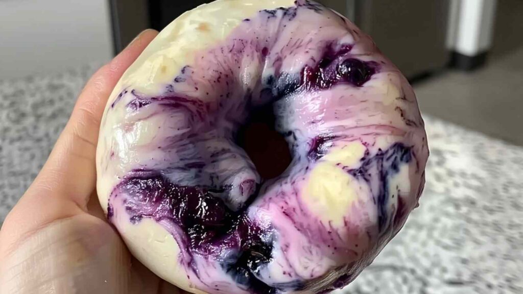 Hand holding raw blueberry bagel dough showing bright purple and blue swirls from fresh berries.