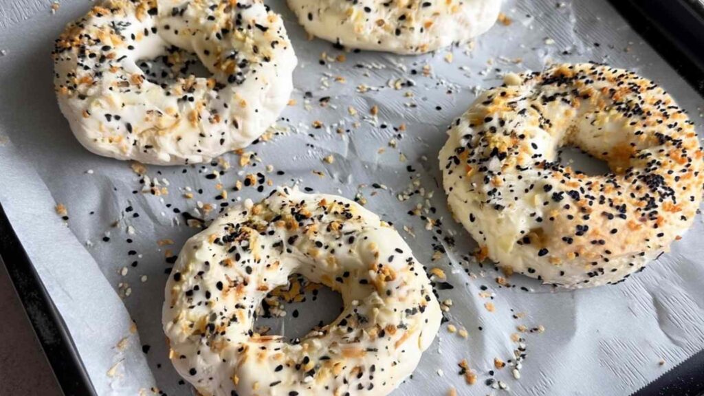 Unbaked Greek yogurt bagel dough rounds on a tray topped with everything bagel seasoning.