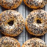 Golden brown onion bagels coated with everything seasoning, cooling on a wire rack