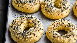 Boiled onion bagels topped with sesame and black seeds on a baking tray, ready to bake