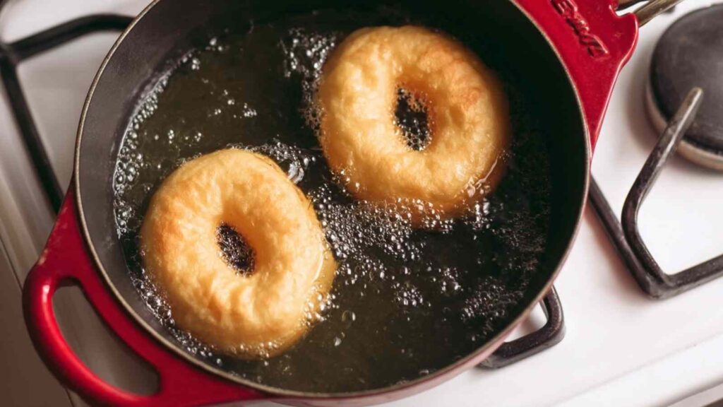 Two sourdough protein bagels boiling in a red pot of water on the stove