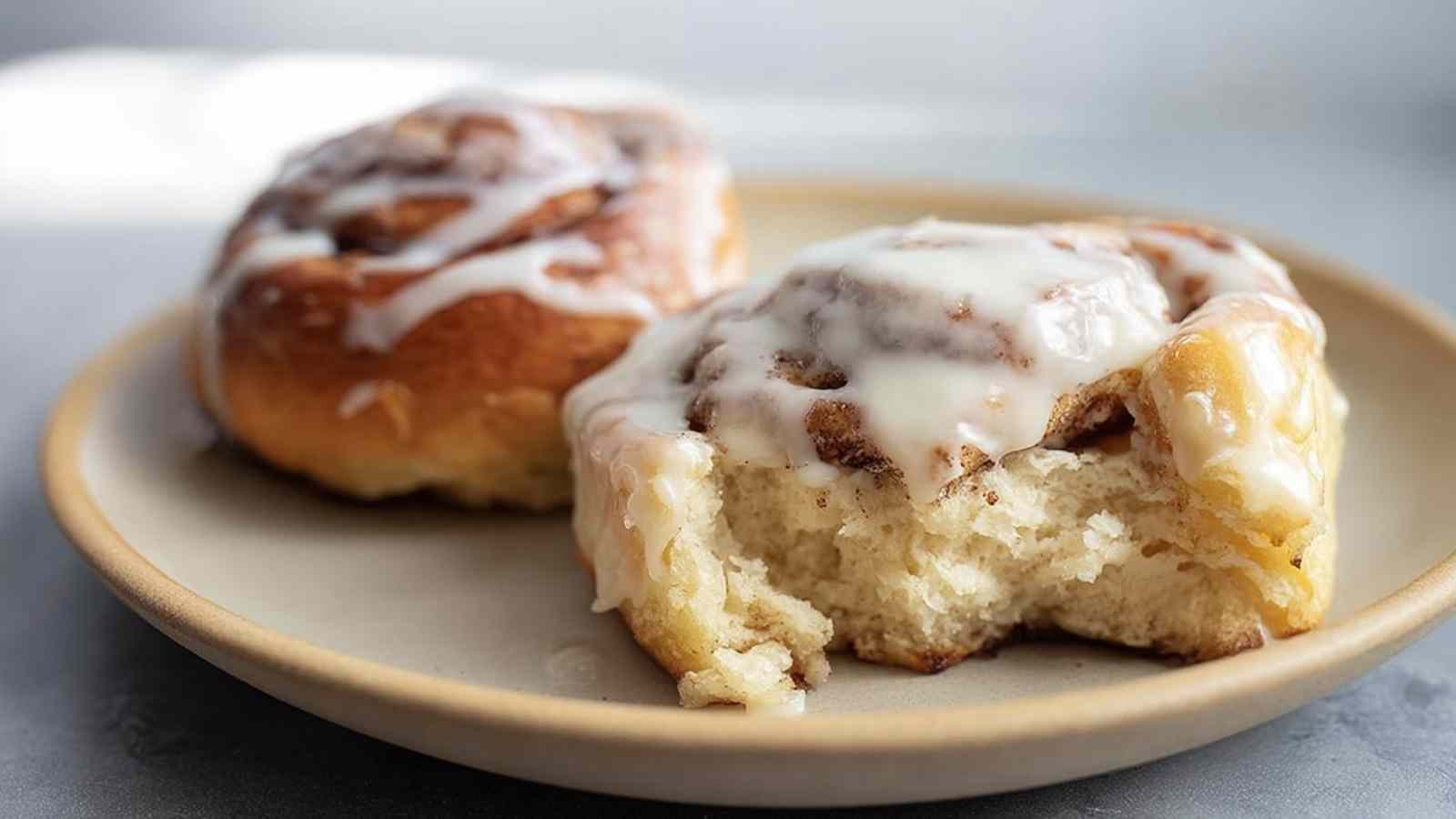 Close-up of a glazed cinnamon roll with a bite taken out, showing the soft interior and gooey cinnamon swirl