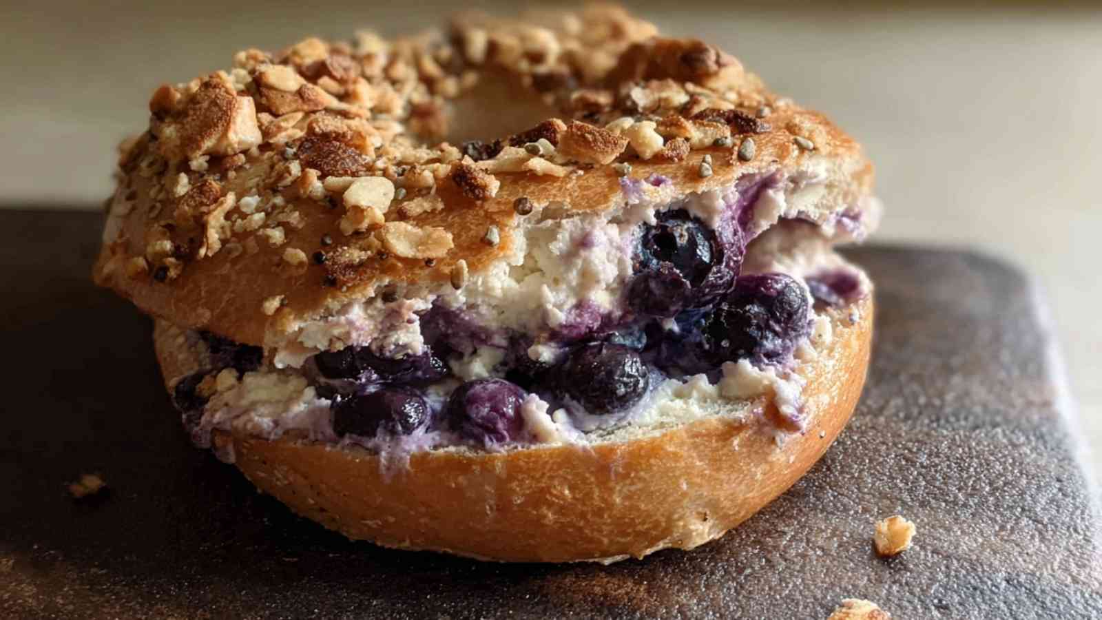 Golden Greek yogurt blueberry bagel topped with almond crumble, filled with fresh blueberries and creamy cottage cheese spread.

