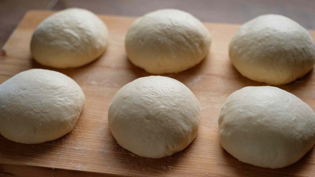 Six smooth, round dough balls resting on a wooden board before final shaping for sourdough baguettes