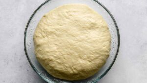 Proofed onion bagel dough in a glass bowl, visibly risen and fluffy