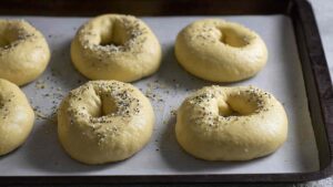 Proofed sourdough discard protein bagels with seasoning on parchment, ready for oven