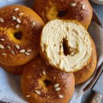 Sourdough pumpkin bagels topped with seeds, one sliced and generously spread with maple pecan cream cheese