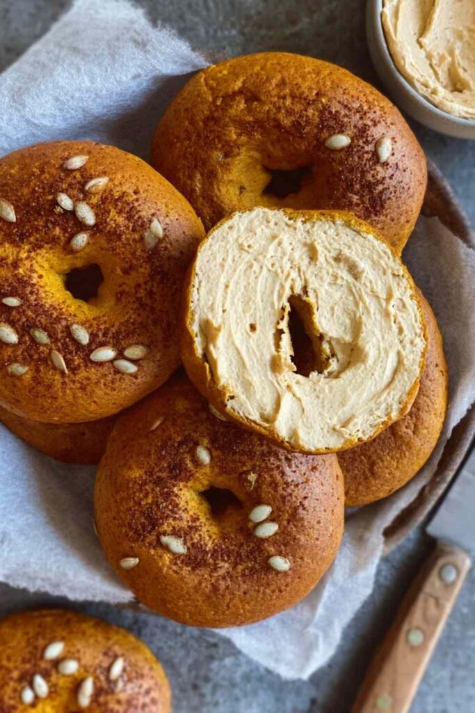 Sourdough pumpkin bagels topped with seeds, one sliced and generously spread with maple pecan cream cheese