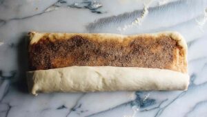 Rolled-up dough log with visible cinnamon-sugar filling on a floured marble surface
