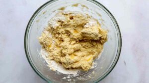 Raw onion bagel dough in a glass bowl, rough and sticky before kneading