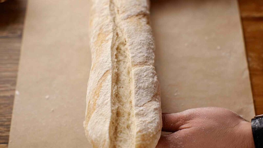 Unbaked sourdough baguette dusted with flour and scored down the center, placed on parchment paper