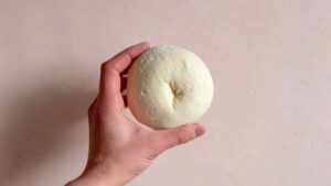 Hand holding shaped sourdough discard protein bagel dough with hole in center