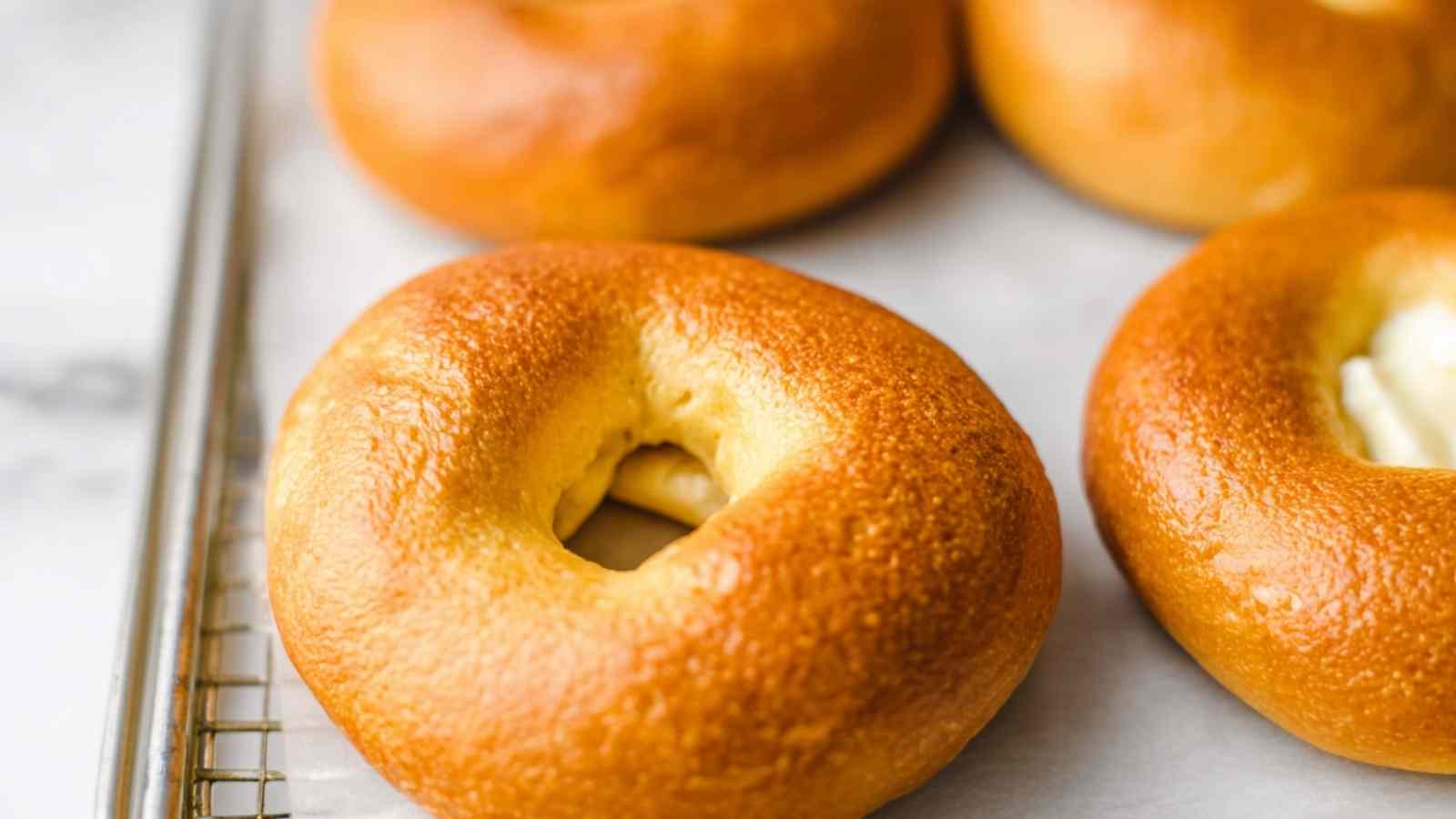 Golden-brown egg bagels resting on a parchment-lined wire rack, baked to a perfect glossy finish