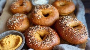 Close-up of golden sourdough pumpkin bagels topped with everything seasoning, served with pumpkin cream spread on a tray