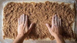 Hands pressing brown sugar cinnamon filling into rolled-out sourdough dough