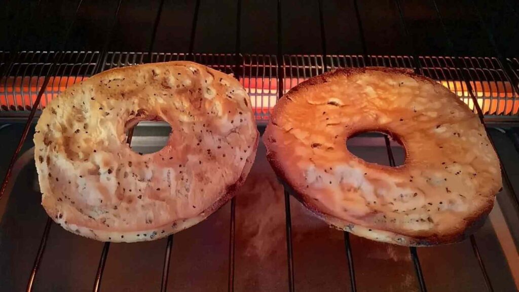 Two Za'atar bagels browning under the broiler in an oven, showing the crisping texture.