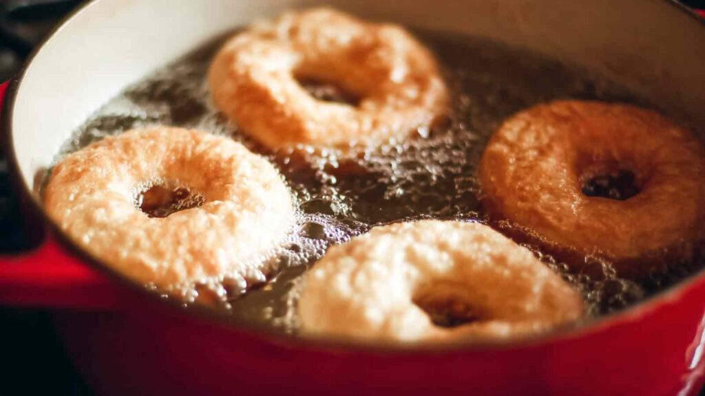 Bagels boiling in a red pot with bubbling water, part of Paul Hollywood's bagel method.