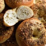 Stack of warm Za'atar Bagels on a white plate, one broken open to show the soft, chewy texture inside and the fragrant za'atar topping.