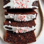 Sliced chocolate peppermint loaf on ceramic plate topped with white frosting and crushed peppermint candy