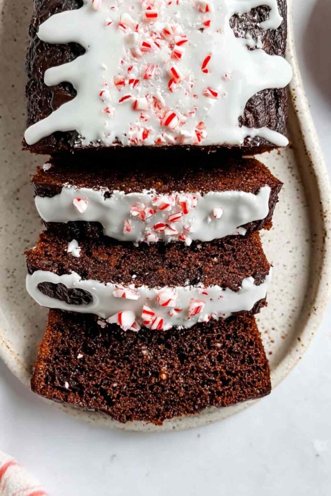 Sliced chocolate peppermint loaf on ceramic plate topped with white frosting and crushed peppermint candy