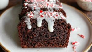 Close-up of chocolate peppermint bread topped with white glaze and crushed candy canes, served on white plate with candy cane pieces