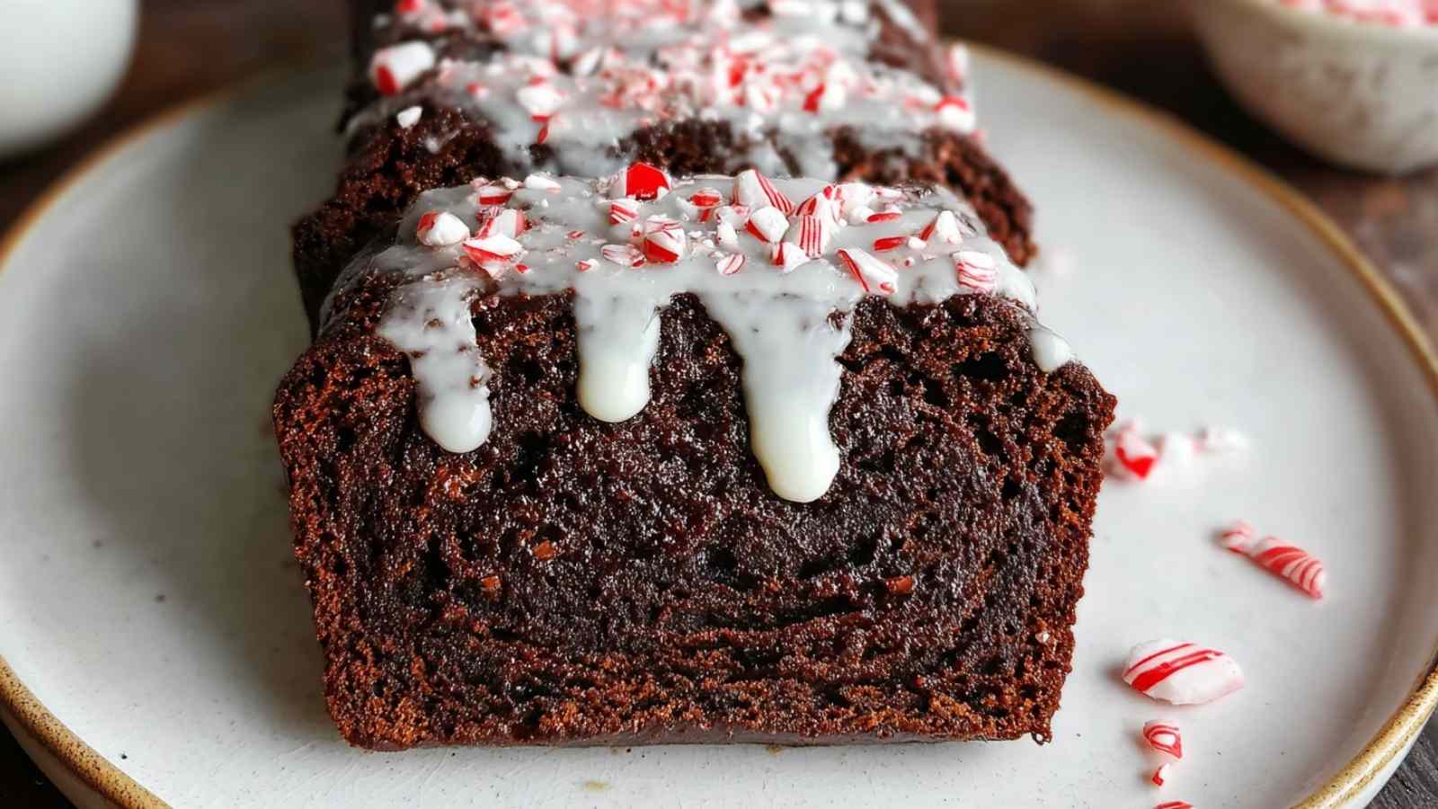Close-up of chocolate peppermint bread topped with white glaze and crushed candy canes, served on white plate with candy cane pieces
