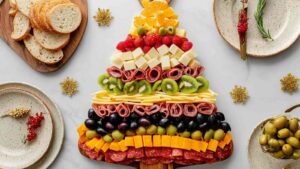Christmas charcuterie board styled like a holiday ornament with layered rows of cheese cubes, grapes, berries, meats, and fresh rosemary on wood board