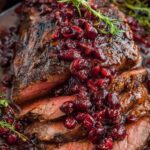 Cranberry balsamic roast beef sliced in a cast iron pan, topped with whole cranberries and a sprig of rosemary, surrounded by a rich sauce.