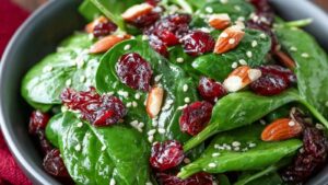 Bowl of spinach salad tossed with dried cranberries, sliced almonds, and sesame seeds—bright red and green colors for the holidays.