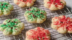 Snowflake-shaped spritz cookies decorated with red, green, and pink sanding sugar on a cooling rack—festive and buttery holiday treats. Snowflake-shaped spritz cookies decorated with red, green, and pink sanding sugar on a cooling rack—festive and buttery holiday treats.