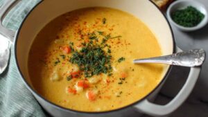 Creamy vegan carrot potato soup in white bowl with fresh herbs