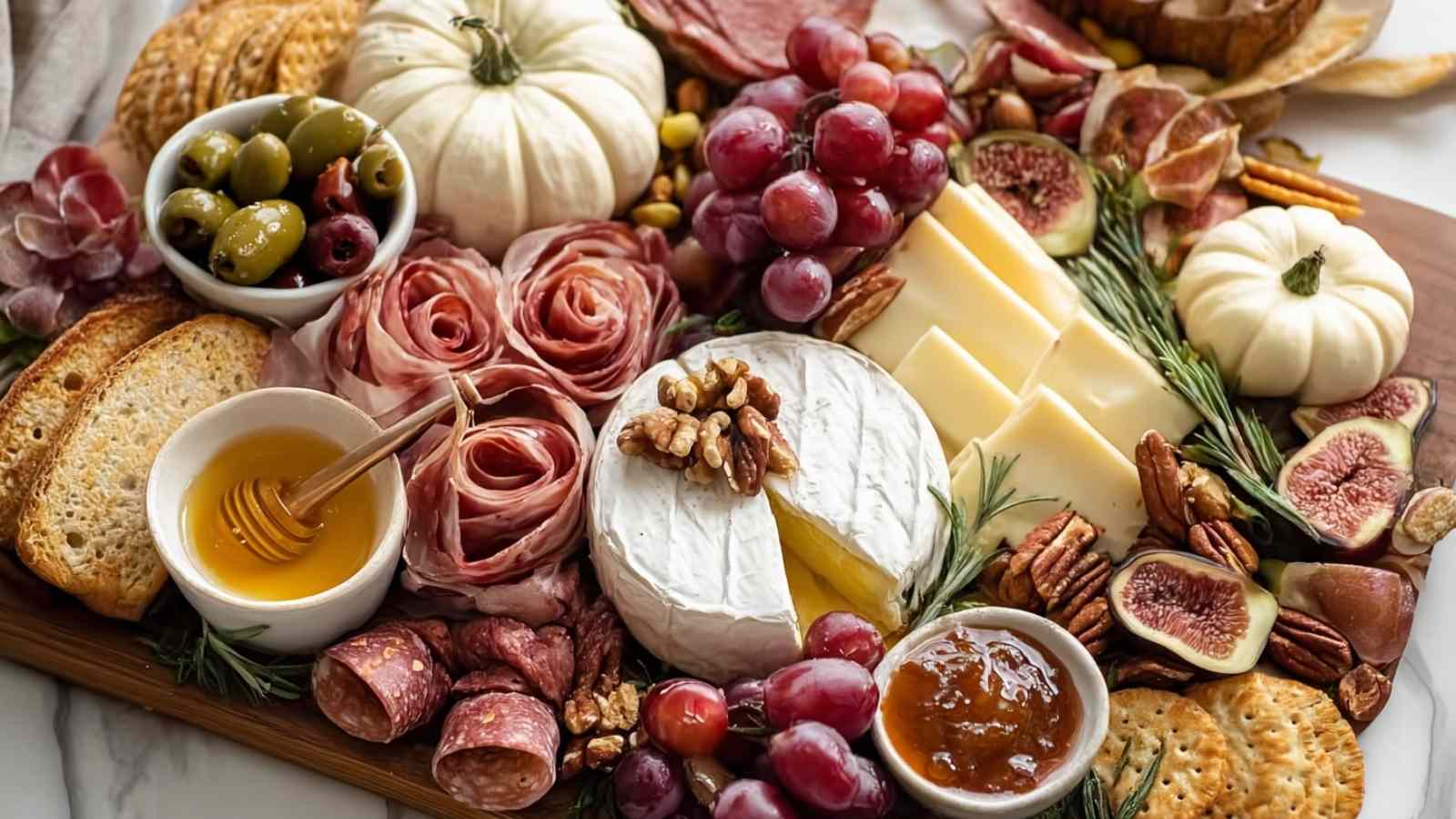 Horizontal view of a fall charcuterie board with brie cheese, figs, grapes, cured meats, and white pumpkins, styled on a wooden board