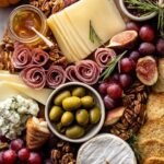 Top-down view of a fall-themed cheese and charcuterie board featuring golden pumpkins, grapes, olives, nuts, and meats
