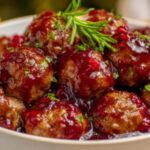 Close-up of cranberry-glazed beef meatballs topped with fresh dill, served in a white bowl—perfectly browned and coated in a rich, glossy sauce.