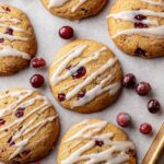 Golden brown cranberry orange cookies drizzled with orange glaze and scattered with sugared cranberries on baking tray