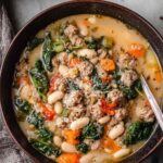 Italian sausage and white bean soup in rustic bowl with herbs