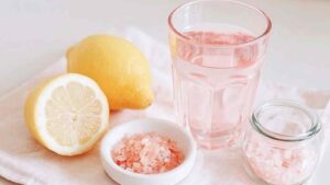 Glass of pink salt lemon water next to lemon halves and pink Himalayan salt in a bright morning setting