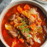 Beef cabbage soup in white bowl with chunks of tender beef and vegetables