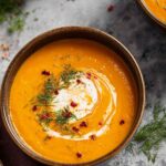 Bowl of creamy carrot and sweet potato soup with cream swirl on top