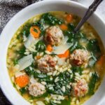 Bowl of Italian wedding soup with mini meatballs, orzo pasta, and spinach garnished with Parmesan cheese