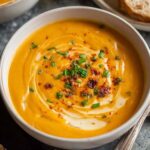 Bowl of creamy sweet potato soup garnished with coconut cream and green onions