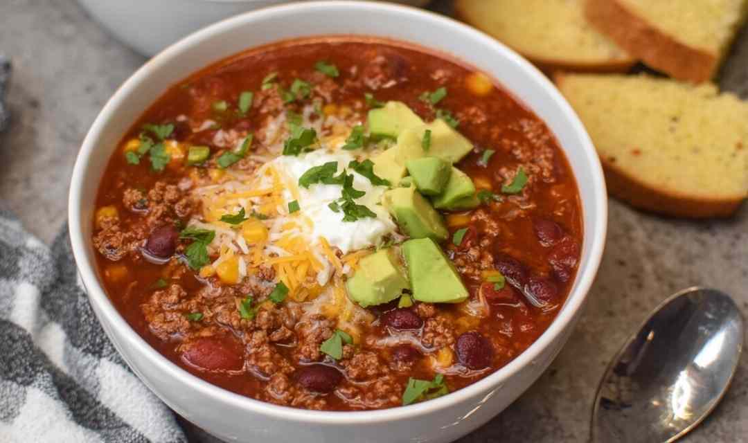 Easy taco soup recipe in white bowl topped with cheese, sour cream, and avocado