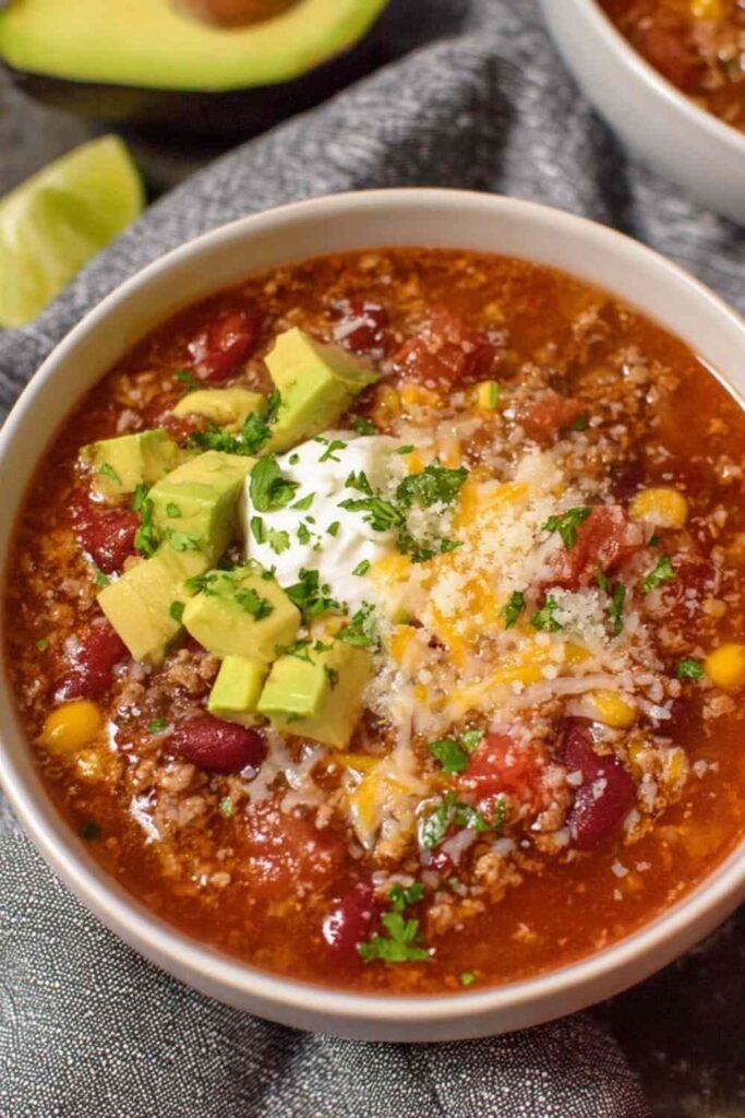 Easy taco soup recipe in white bowl topped with cheese, sour cream, and avocado