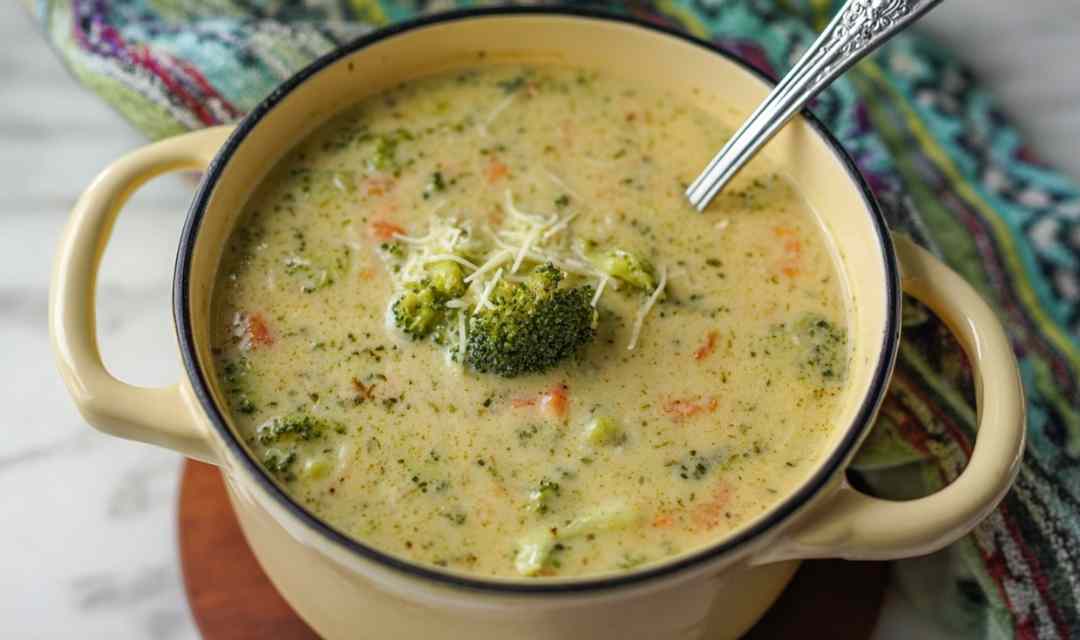 Bowl of high protein broccoli cheddar soup with melted cheese and fresh broccoli florets